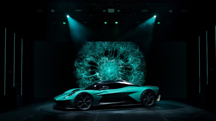 Mint green Aston Martin on a show stand with a graphic pattern in the background