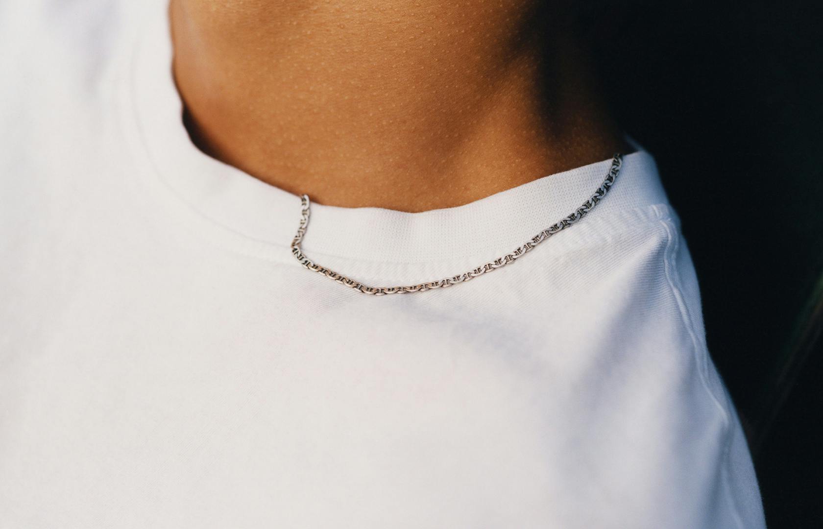 Close-up of a person wearing a thin chain necklace draped over a white t-shirt