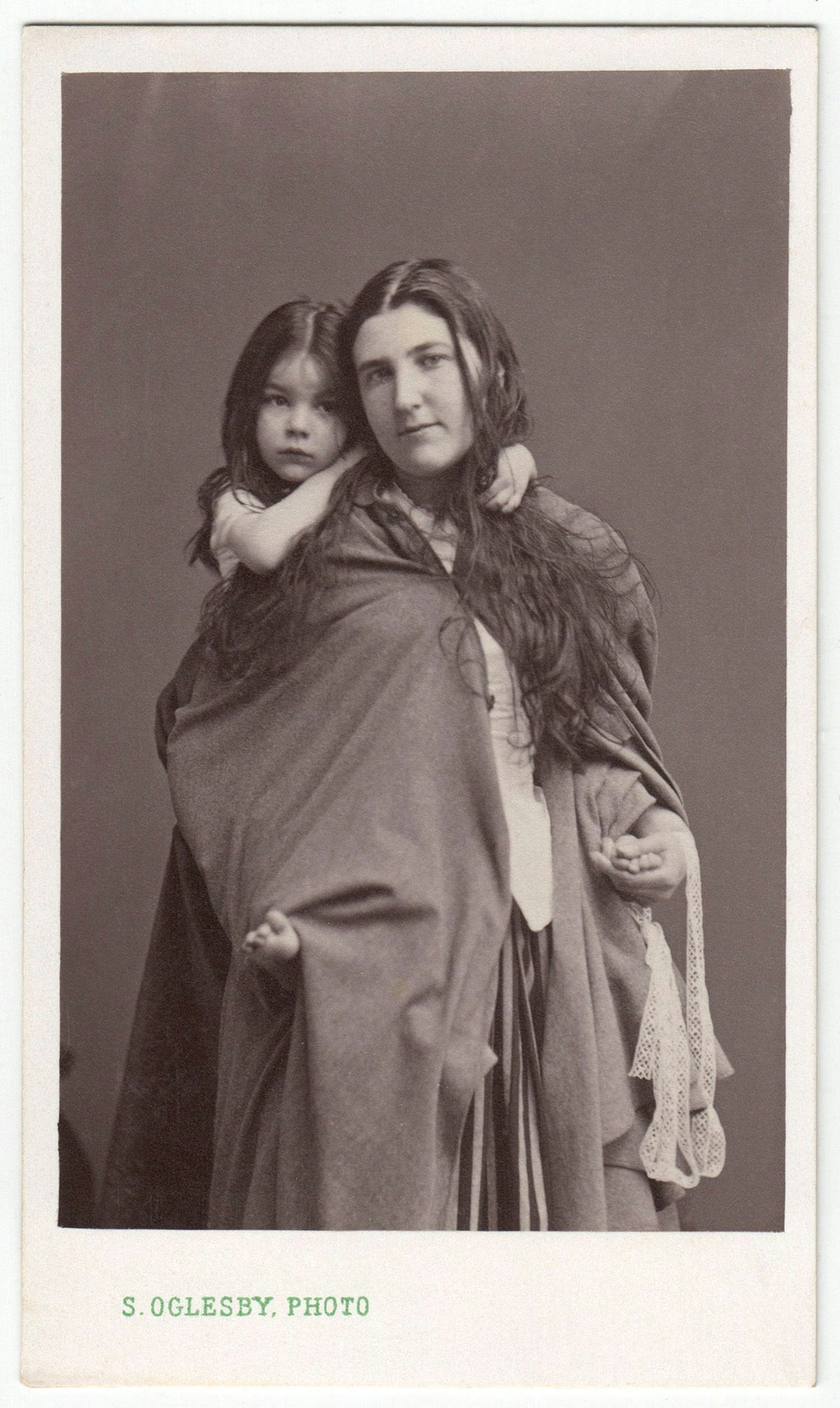Sepia toned photo of a person with long hair and wearing a loose wrap with a child on their back
