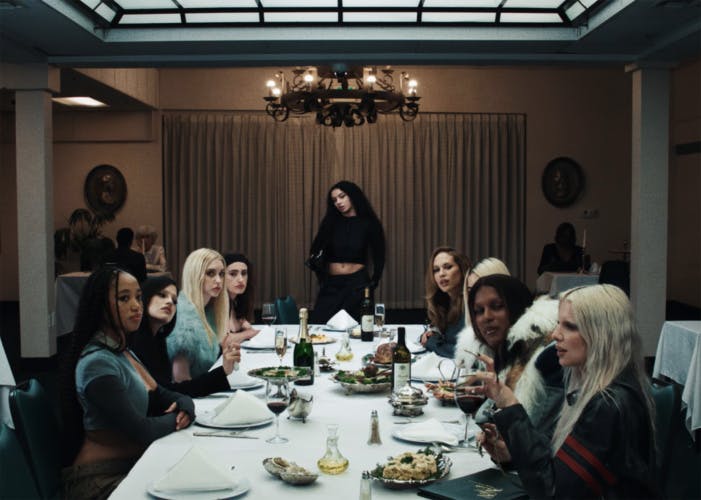 Still from the music video for 360 by Charli XCX, showing Charli standing at the end of a dining table with guests including Rachel Sennott and Julia Fox sat around it