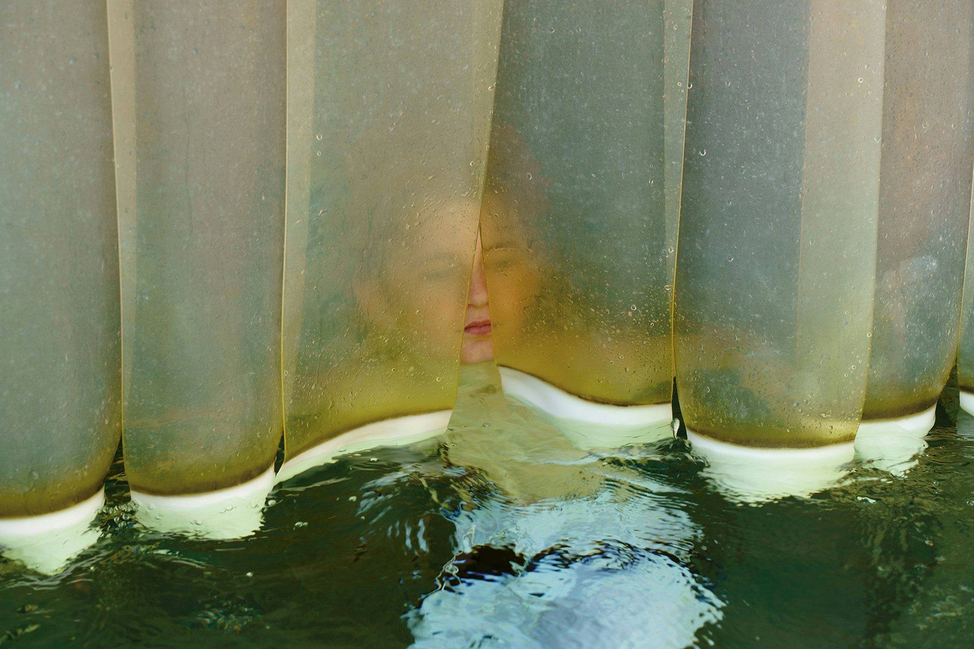 A boy in a pool of water hovering behind a plastic panel curtain