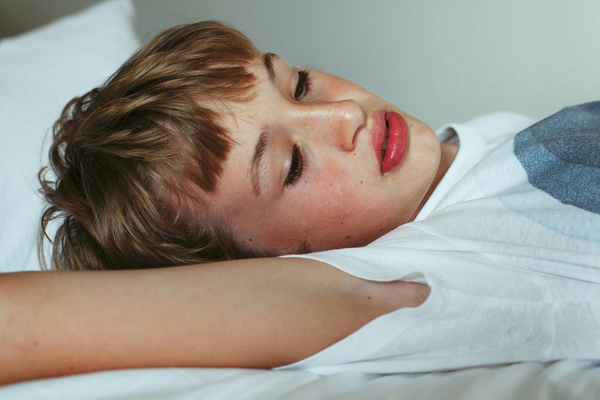 A boy with light brown hear wearing a white t-shirt while lying down
