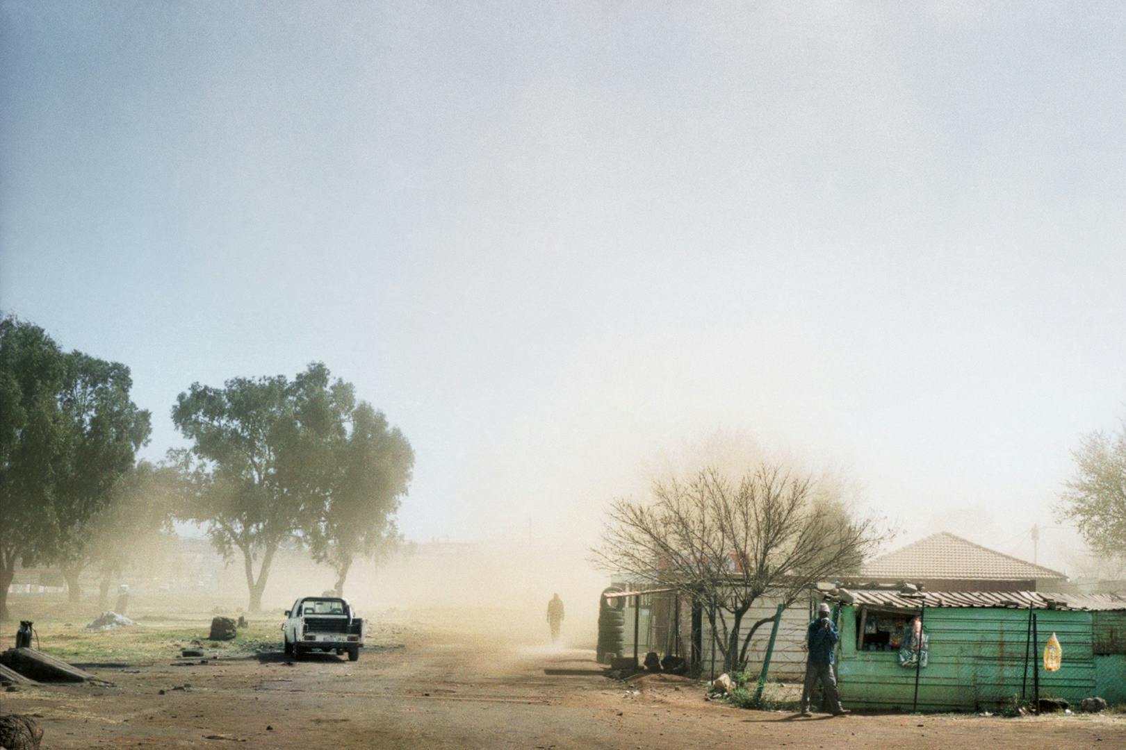 A dusty landscape with a pick up truck and several buildings