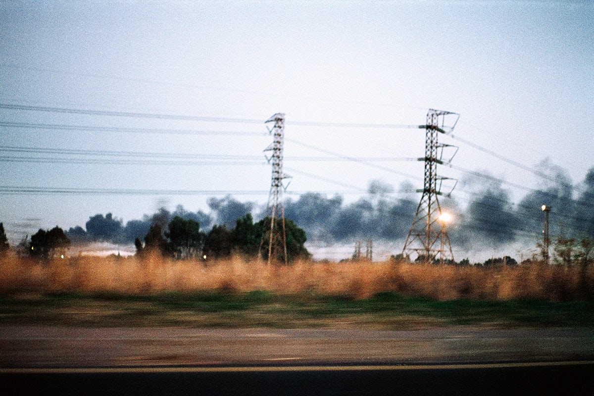 Dark grey clouds or plumes of smoke strewn across a sky at dusk, with two pylons in a field