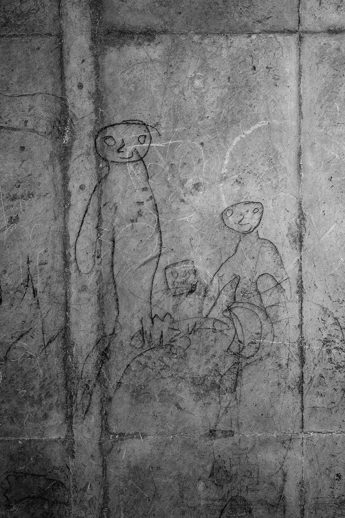 Black and white photo of line drawings of human figures etched on a wall