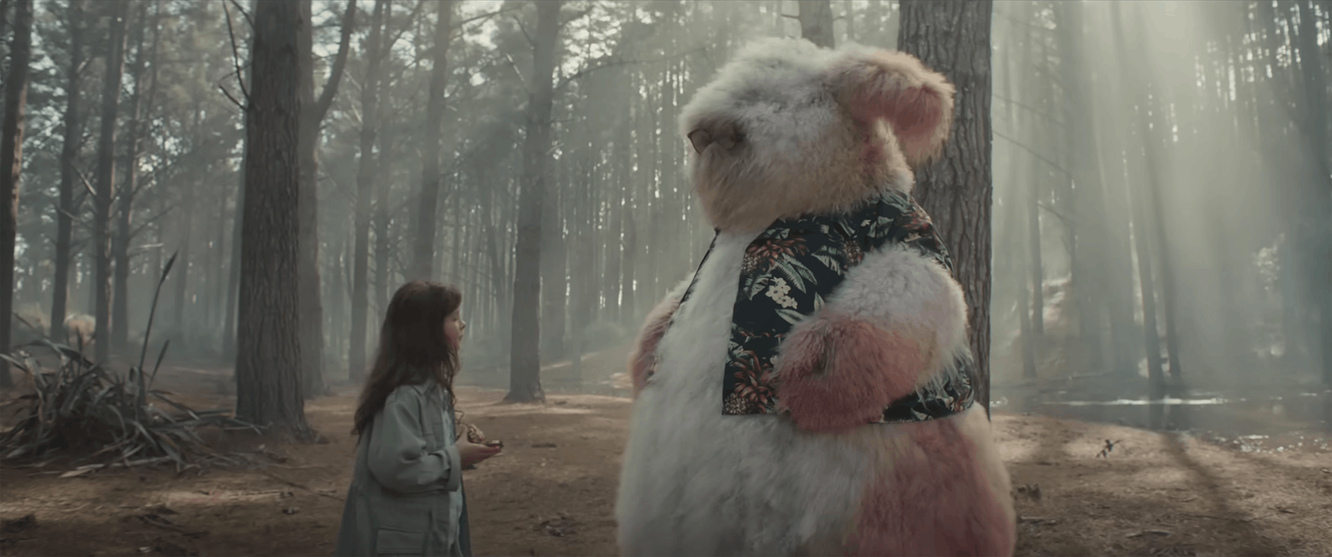 A young girl in a forest standing opposite a large furry creature