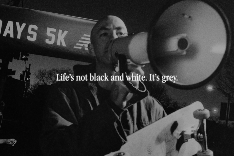 Black and white shot of skateboarder Andrew Reynolds speaking into a megaphone while holding a skateboard. The phrase 'Life's not black and white. It's grey' is laid over the image