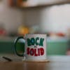A mug on a kitchen table featuring the words Rock Solid in angular red and green letters