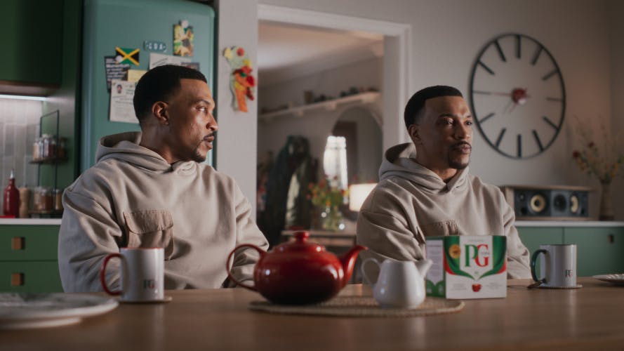 Ashley Walters sat next to another version of himself at a table with a teapot and PG Tips box on top, taken from the brand's new advert