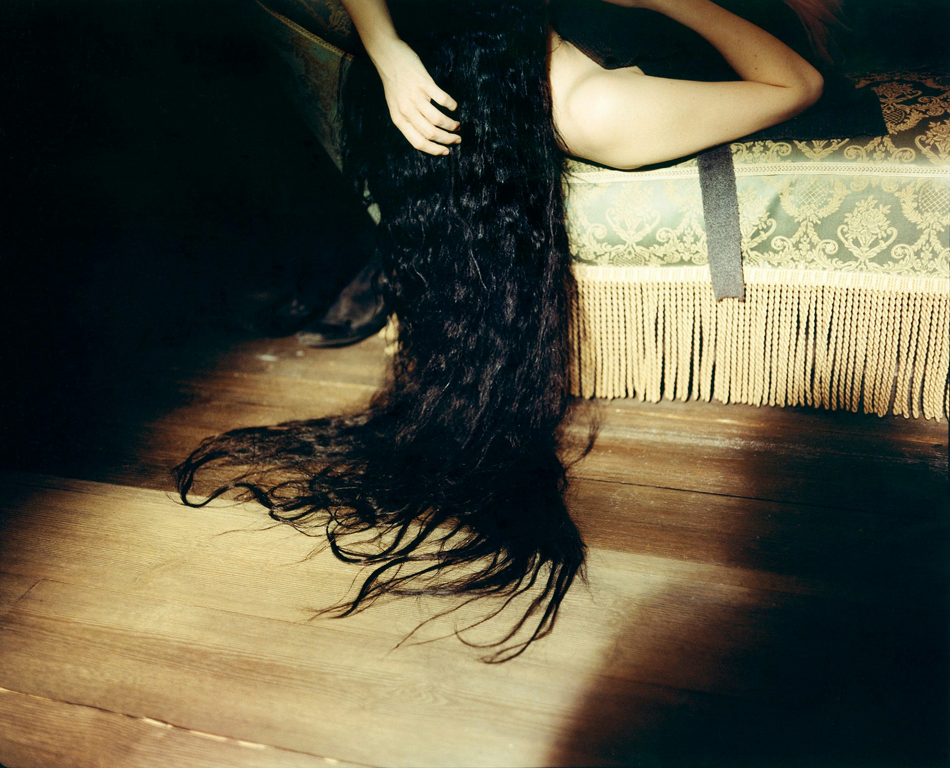 Emma Stone lying on a bed with her very long dark hair draped over the side and pooling on the wooden floor