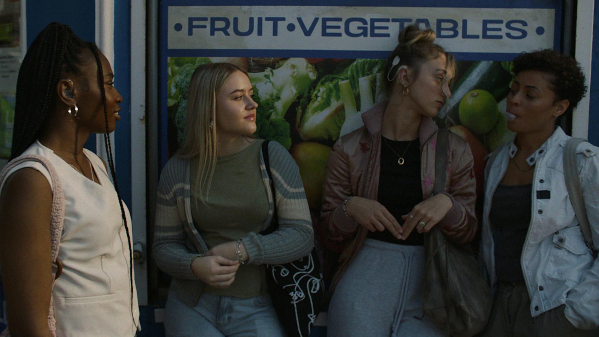 A group of four young people standing outside a fruit and vegetable shop