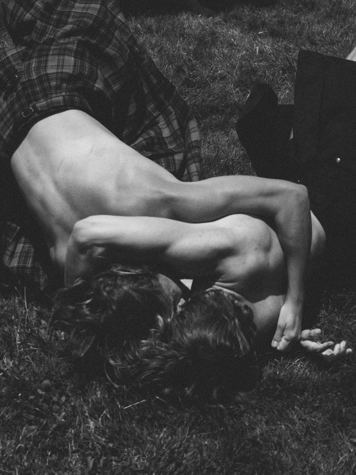 Black and white photo by Robbie Lawrence showing two people wearing kilts and bare chested lying on grass