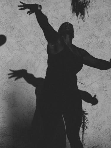 Black and white photo by Robbie Lawrence showing a person with their arms extended, and their shadow projected against a grey backdrop