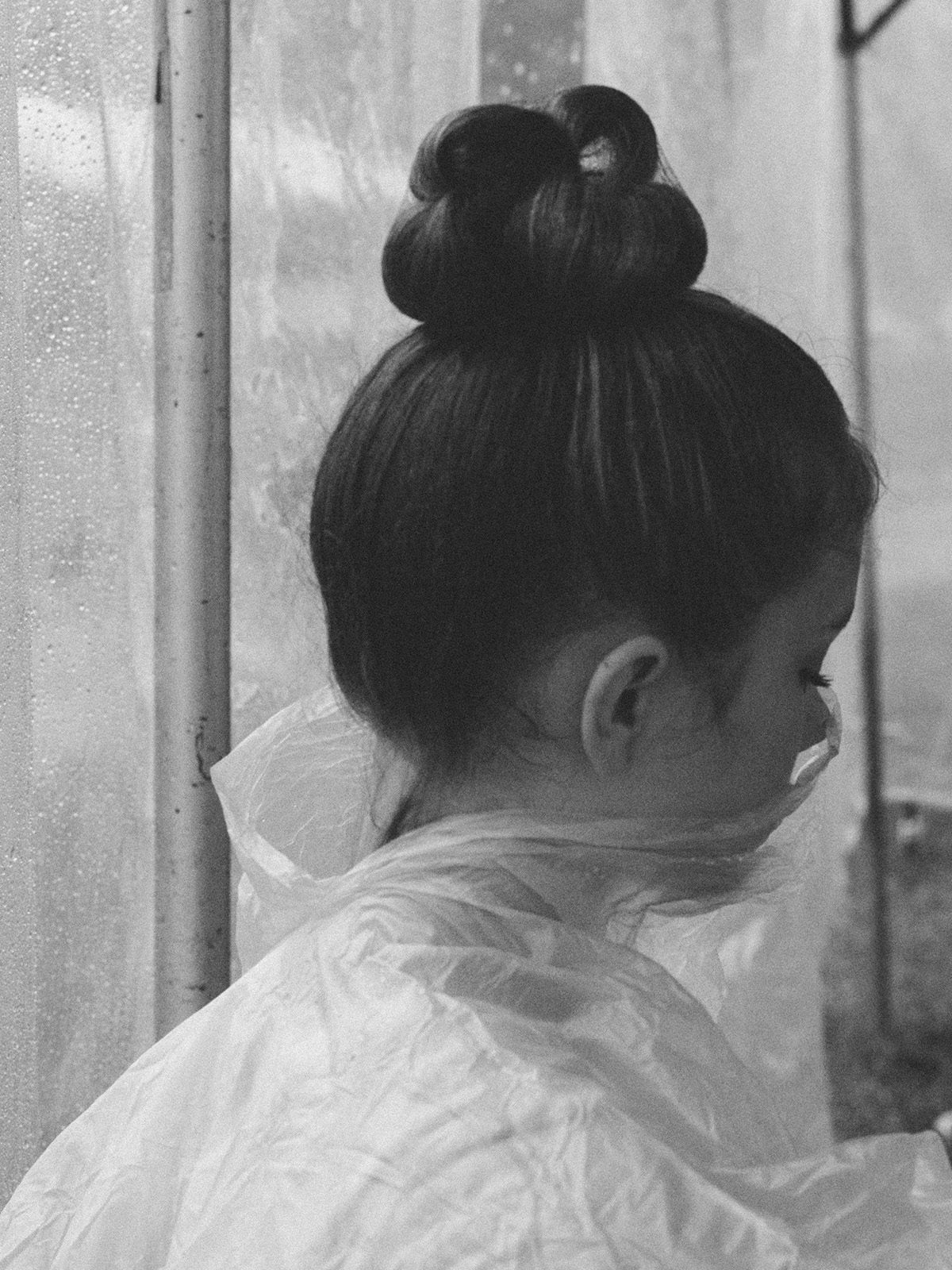 Black and white photo by Robbie Lawrence showing a young person with their hair in a high bun wearing a translucent poncho