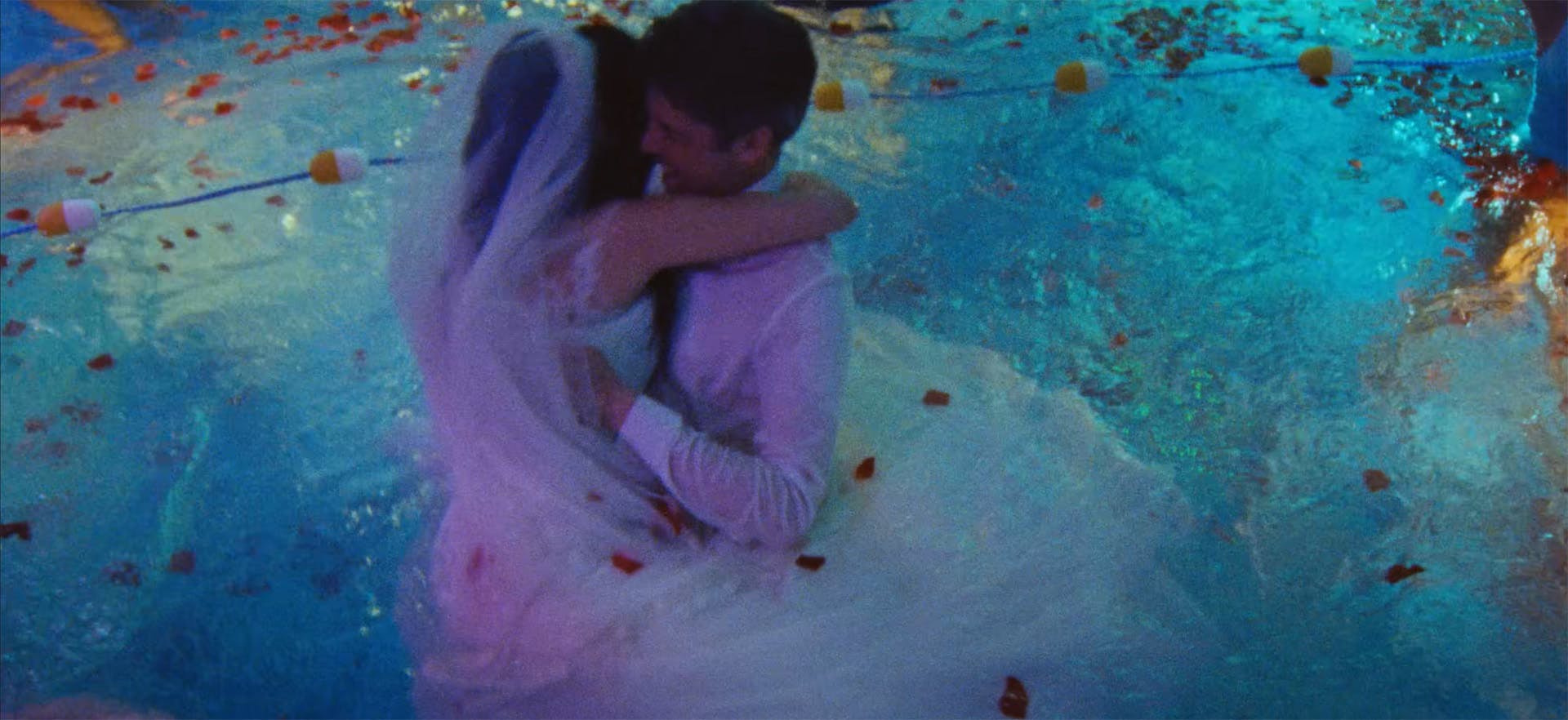 Still from the music video for Treat Each Other Right by Jamie xx, showing a bride and groom embracing in a swimming pool