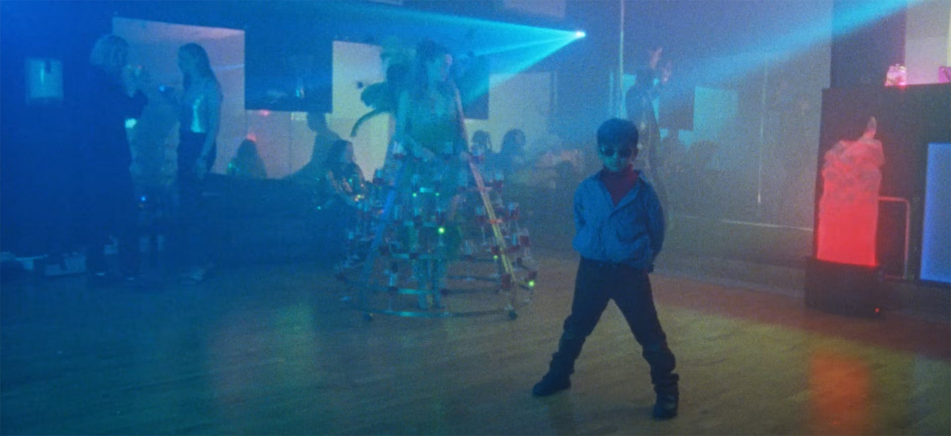 Still from the music video for Treat Each Other Right by Jamie xx, showing a child wearing sunglasses and a windbreaker jacket
