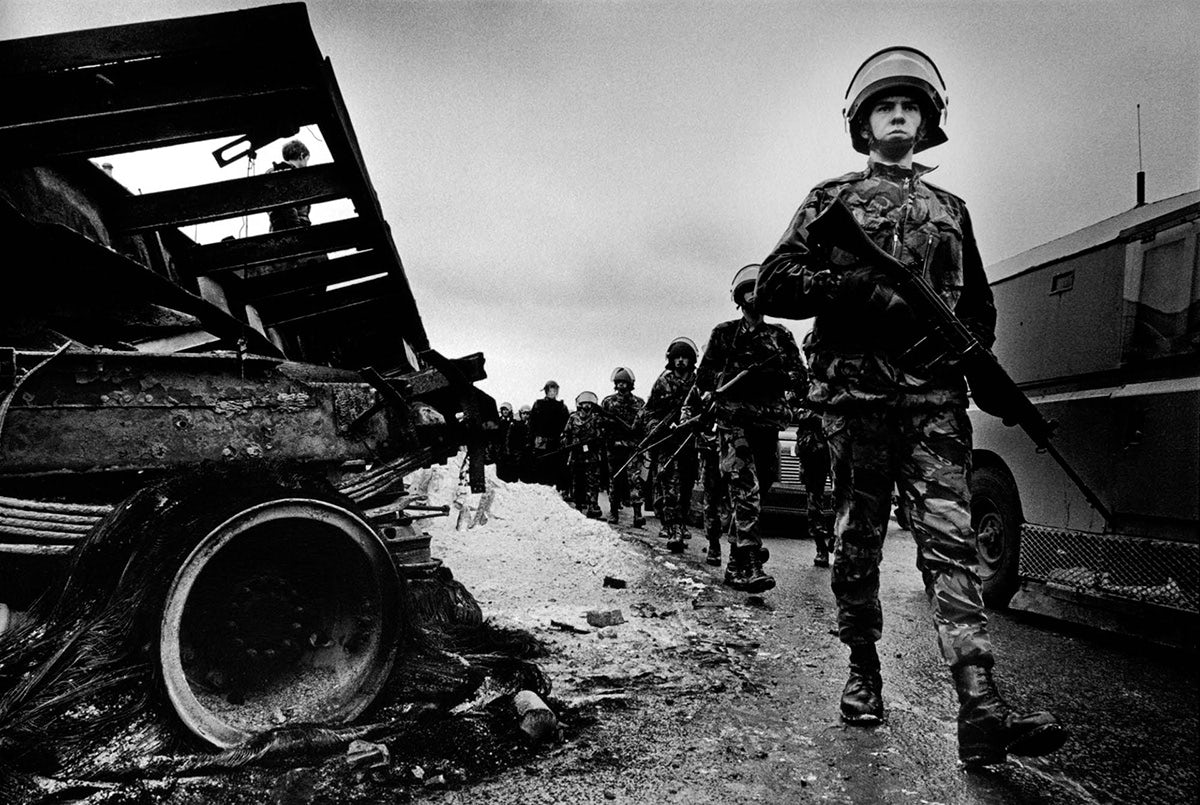Black and white photo of troops holding guns walking marching through a wet street