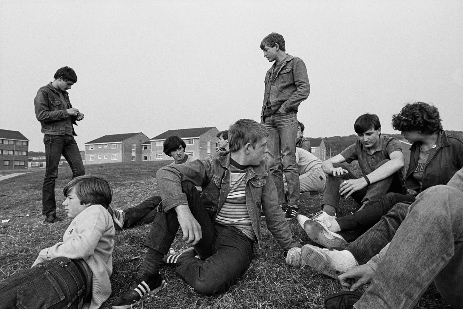 Black and white photo of a group of young adults sat on a grassy mound in front of rows of houses