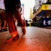 Red hued photograph by Mo Yi of a street scene featuring a person's legs and feet taken near ground level