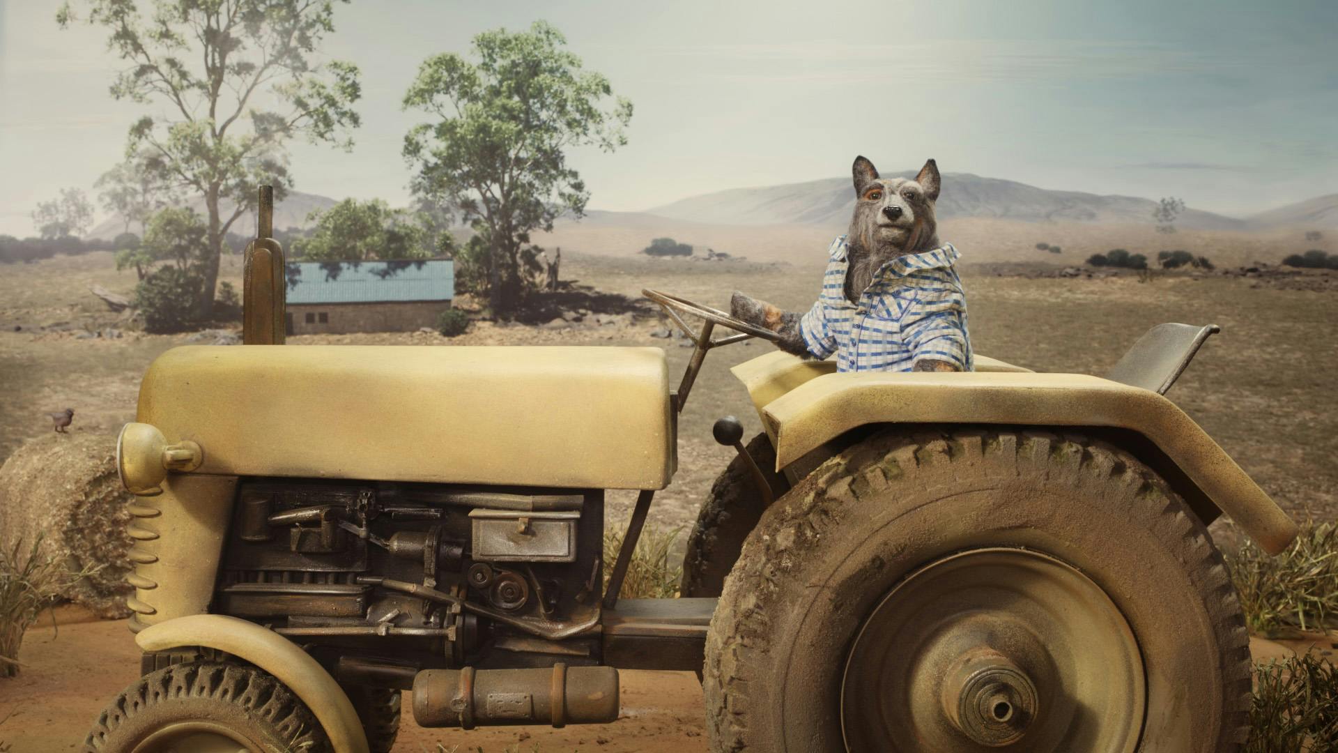 A grey puppet of a creature sitting on a tractor against a model of an Australian landscape