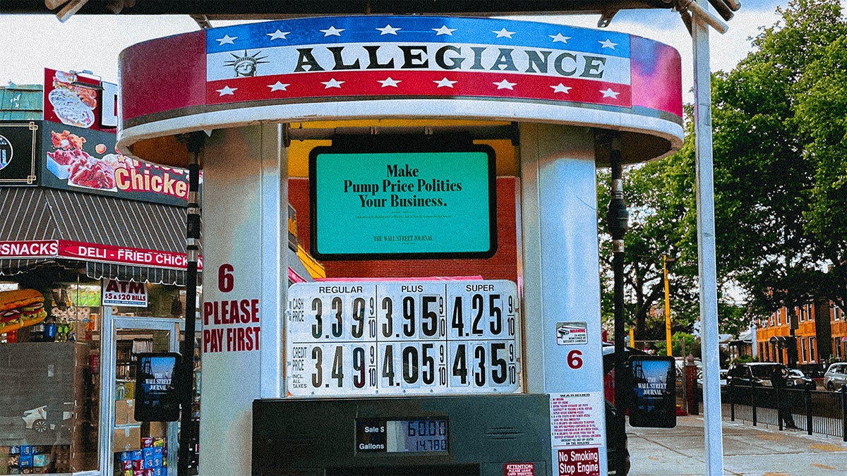 Wall Street Journal ad that reads 'make pump price politics your business' displayed on a stand next to fuel prices
