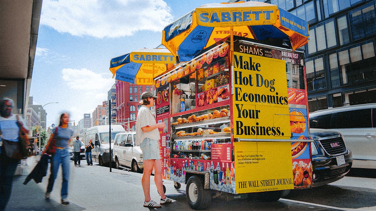 Wall Street Journal ad that reads 'make hot dog economics your business' displayed on the side of a hot dog cart in a city street