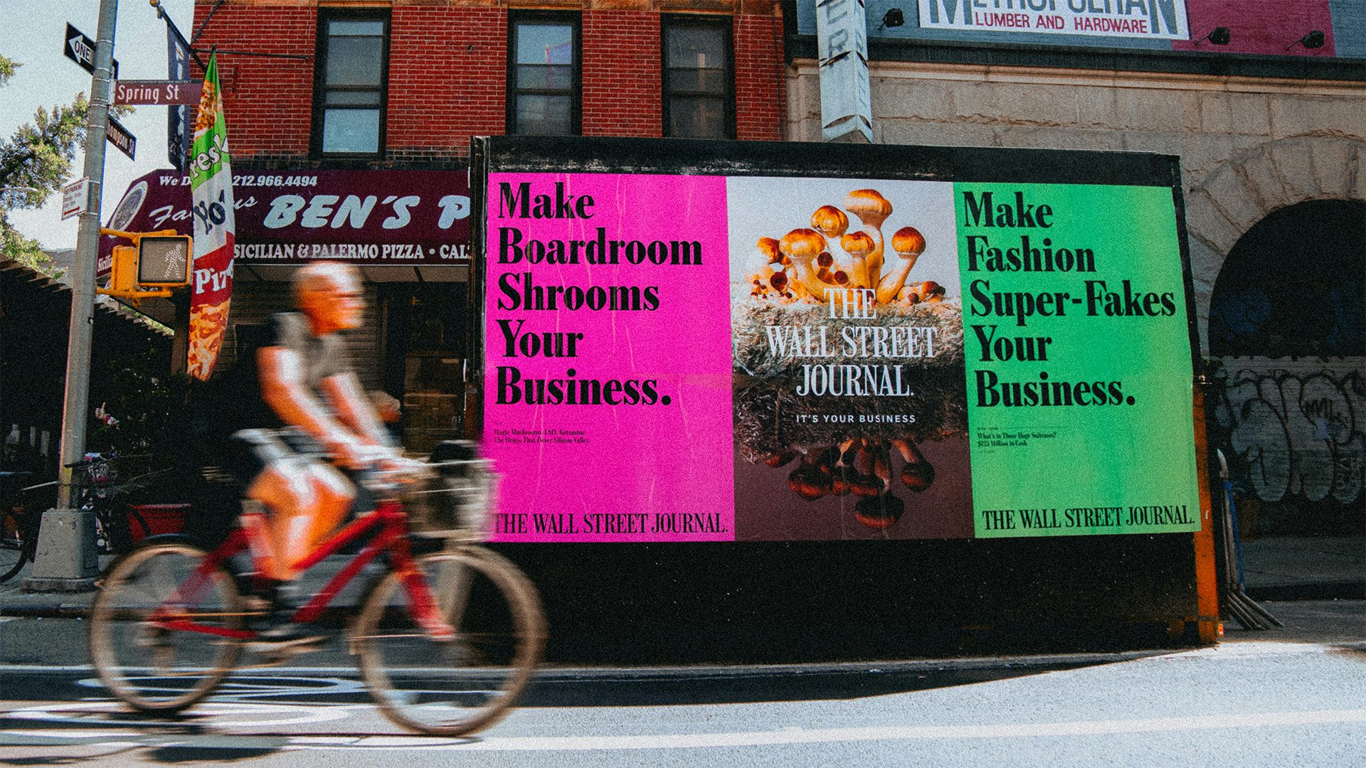 Wall Street Journal ads that read 'make boardroom shrooms your business' displayed on a stand in a city street as a cyclist rides past