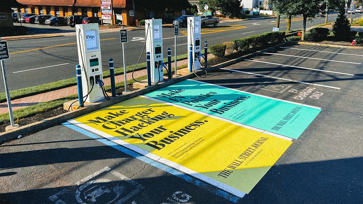 Wall Street Journal ads painted on a parking spot next to an electric vehicle charging station. The ads read 'make charger hacking your business' on colourful backgrounds