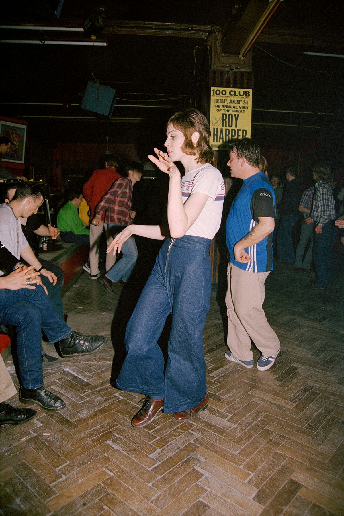 A person wearing large flared trousers in a hall surrounded by people