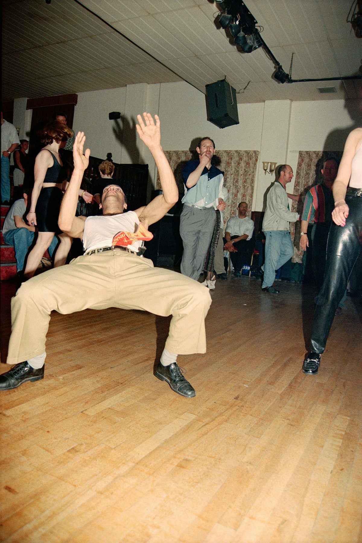 People dancing in a hall, including one person leaning backwards with hands in their air