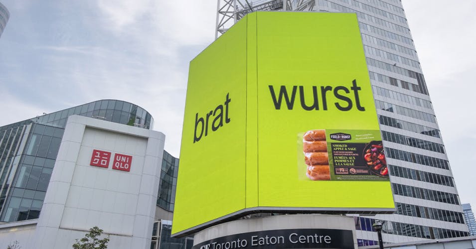 Billboard that features the words 'brat' and 'wurst' alongside a photo of a pack of sausages, against a bright green background and fuzzy lowercase letters in the style of Charli XCX's Brat album cover