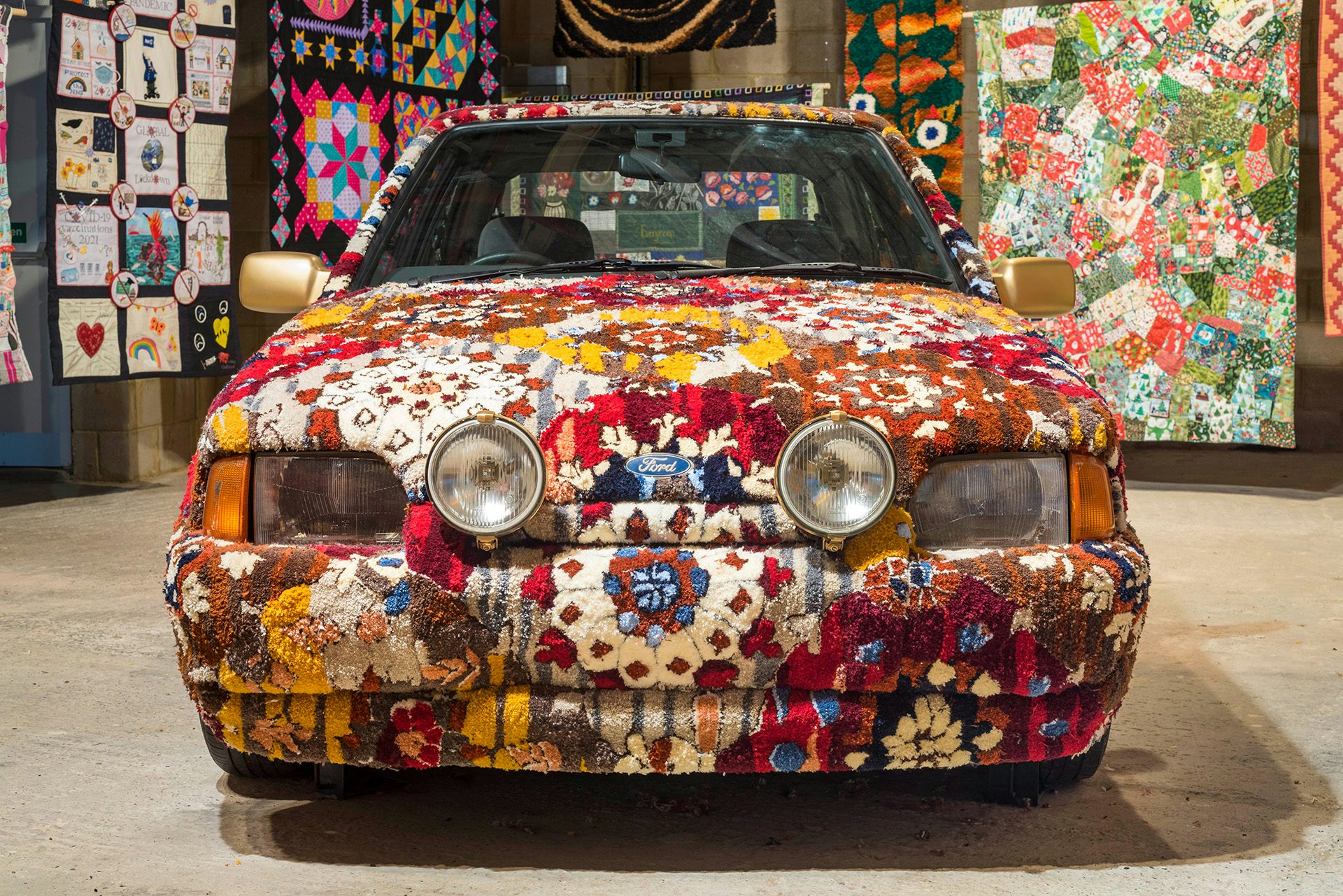 Exhibition installation of a car body made out of floral textiles, with textiles draped in the background
