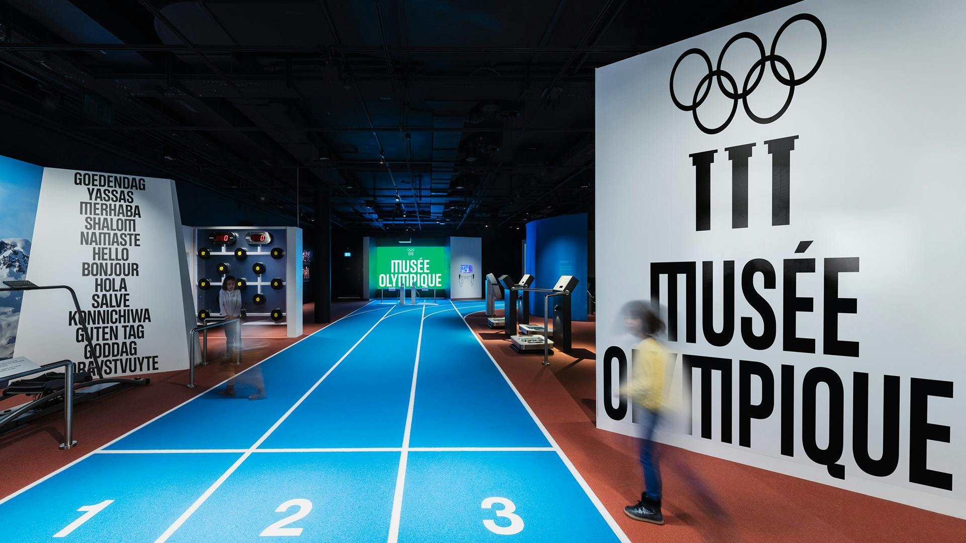 A room inside the Olympic Museum featuring floor markings inspired by a running track, and large displays featuring the new brand identity