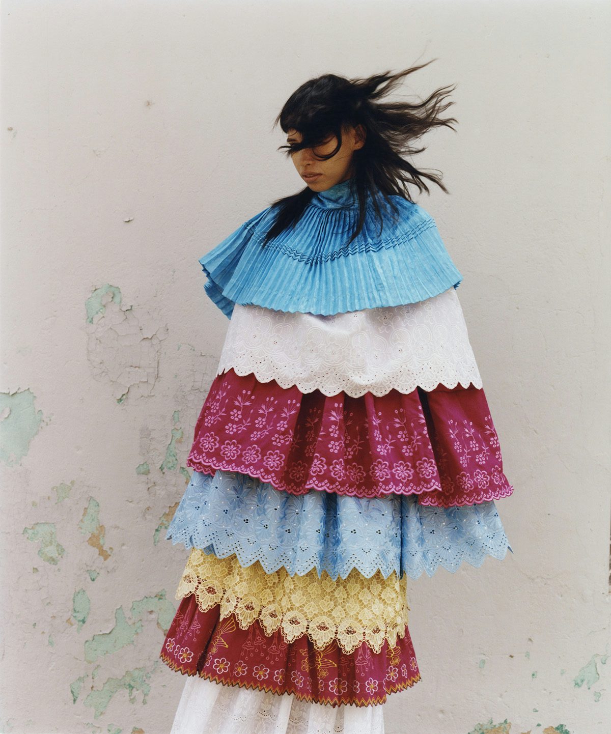 Photo by Ana Margarita Flores of a person with their hair blowing across their face and wearing a blue, white, yellow and red tiered garment