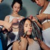 Three women standing around a young woman as they do her hair and make-up