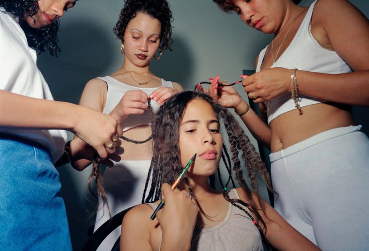 Three women standing around a young woman as they do her hair and make-up