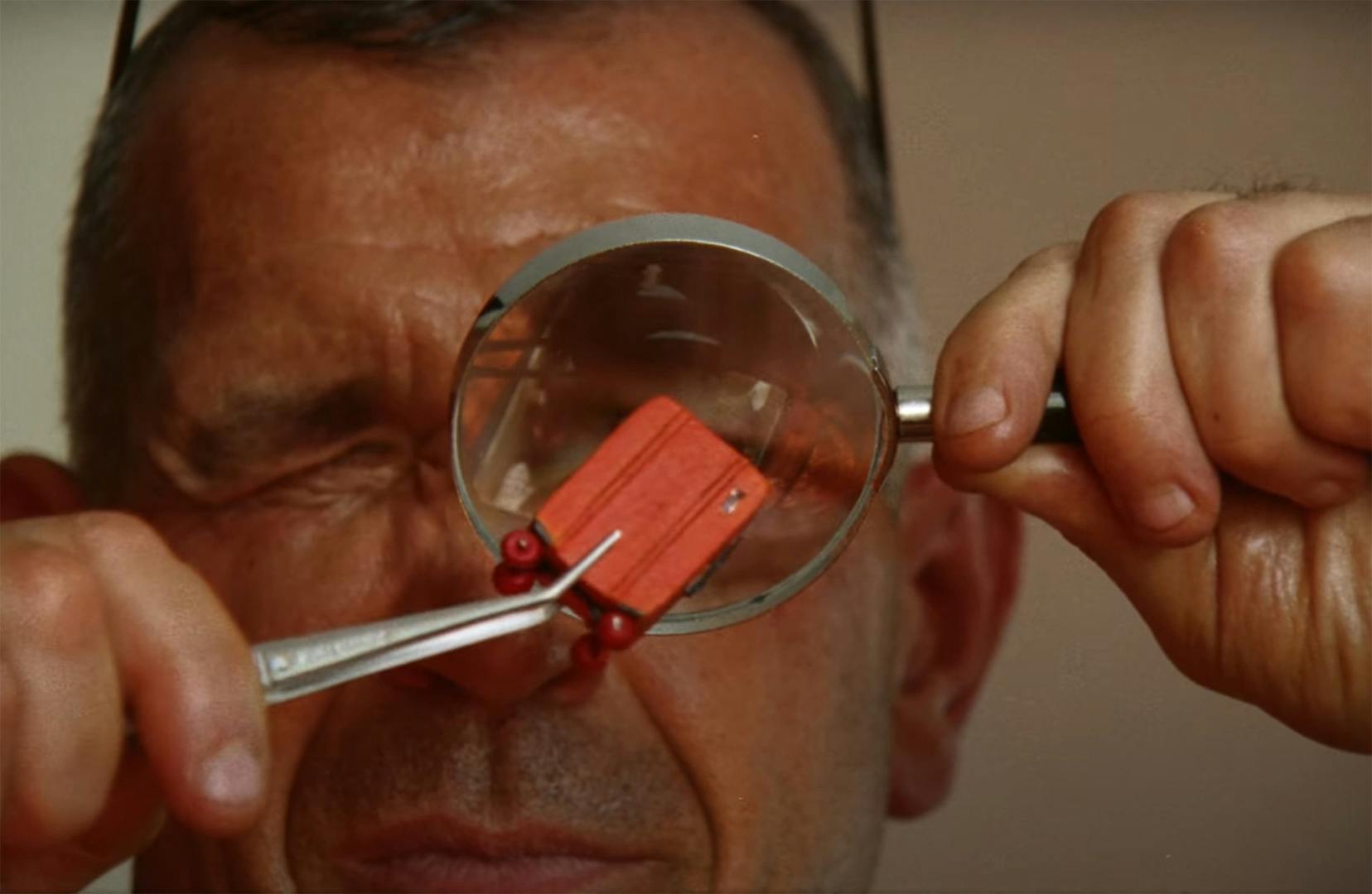 A close up of a man inspecting a miniature suitcase through a magnifying glass