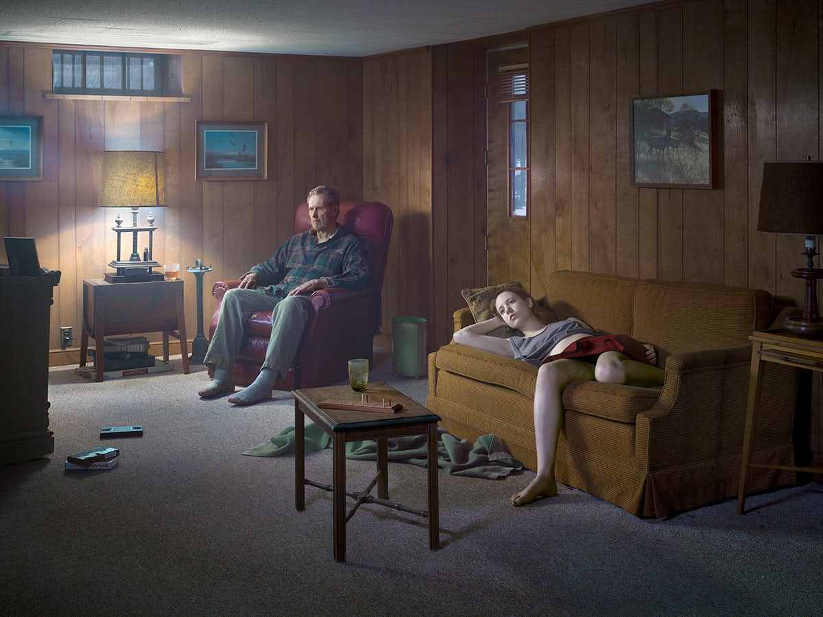 A person sat in an armchair and another person lounging on a mustard sofa in a wood panelled room, both gazing ahead into the distance
