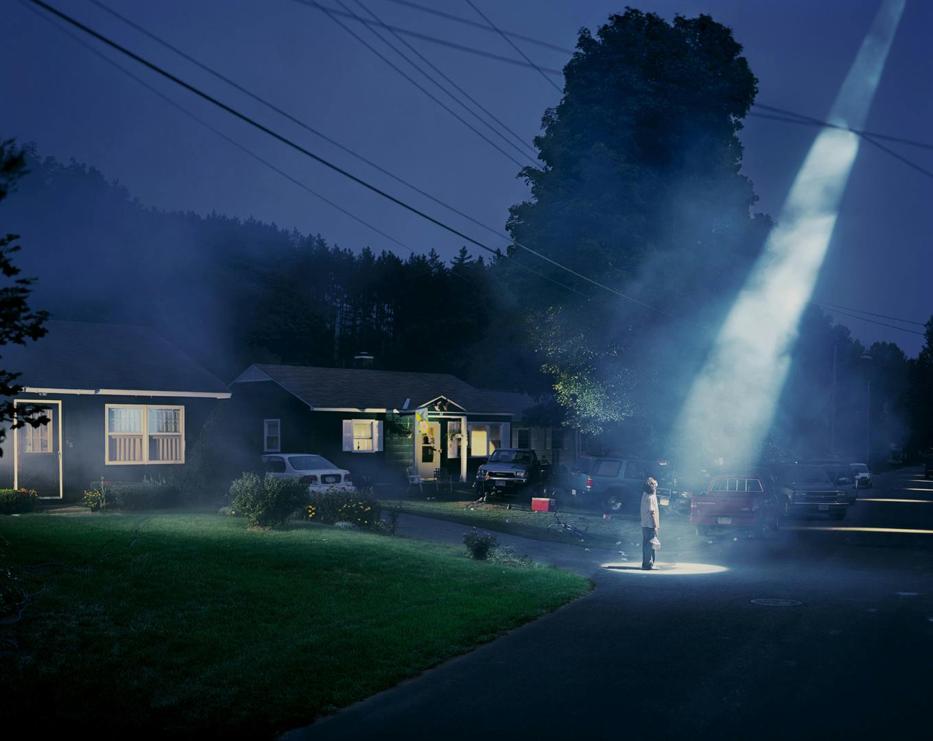 A person standing outside a row of suburban bungalows at nighttime with a beam of light cast down on them