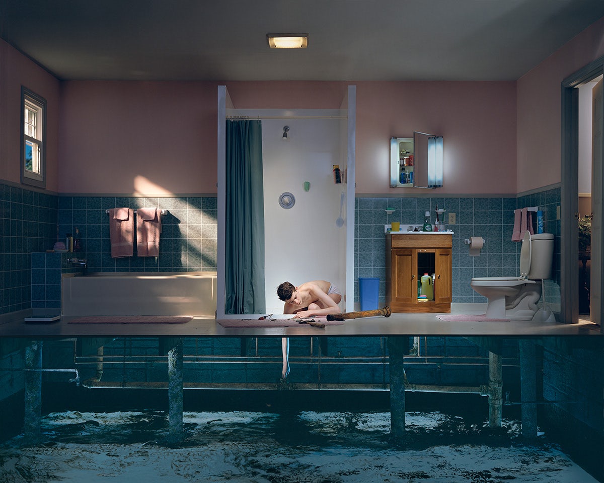 A person in a bathroom appearing to be crouched in a shower cubile reaching beneath the floor panels. The side of the scene has been cut away as though a dolls house