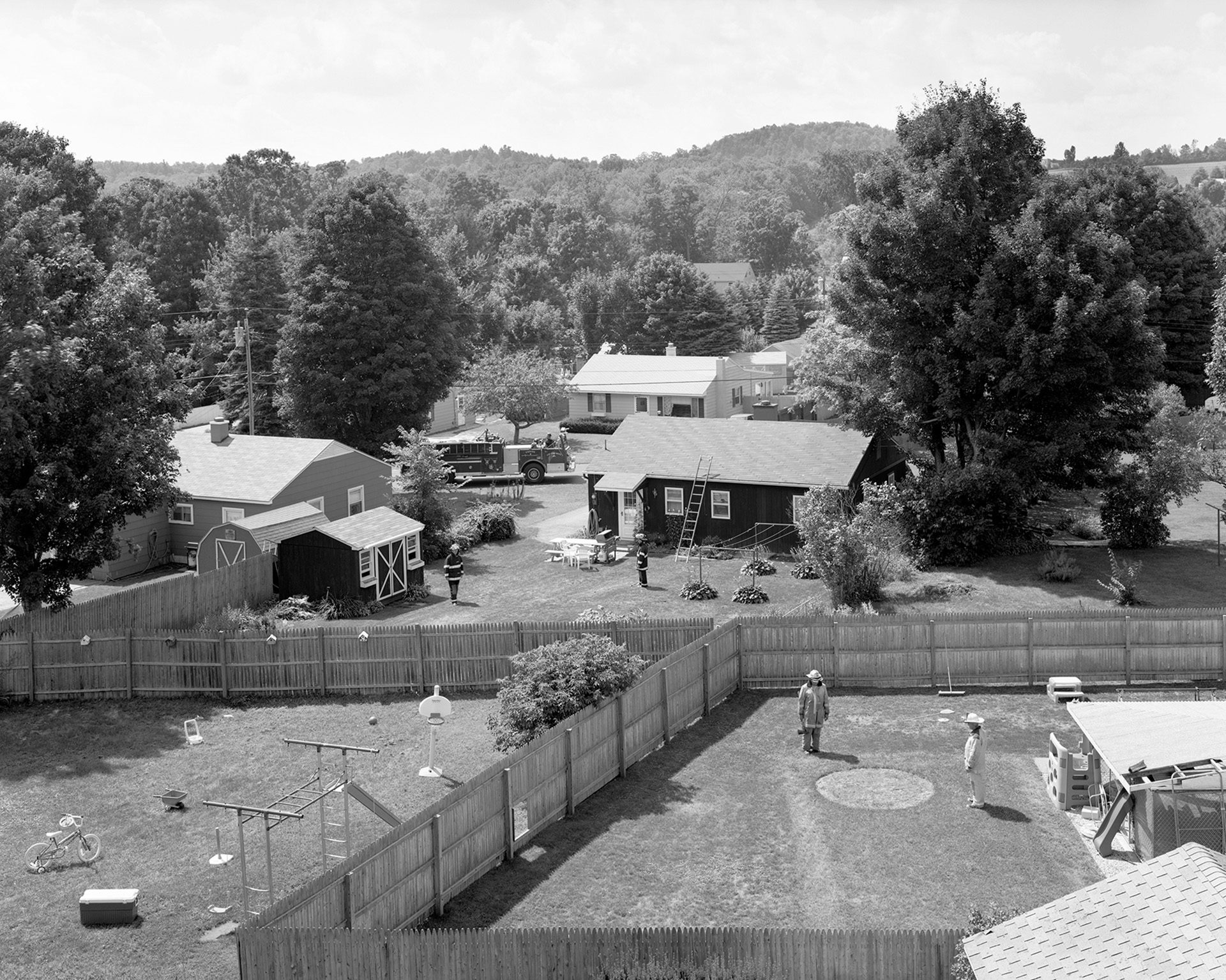 Black and white photo by Gregory Crewdson of a group of back yards divided by fences