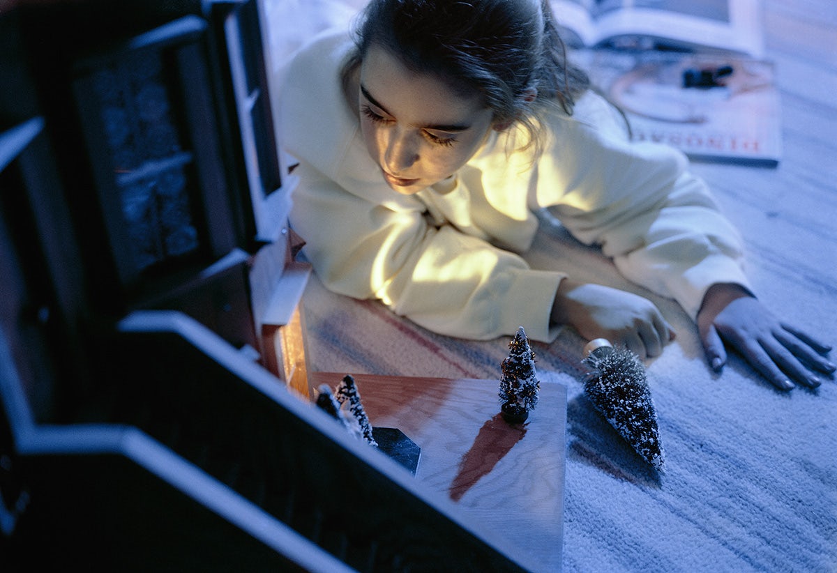 A blue toned photo of a person gazing at a model of a snow covered house