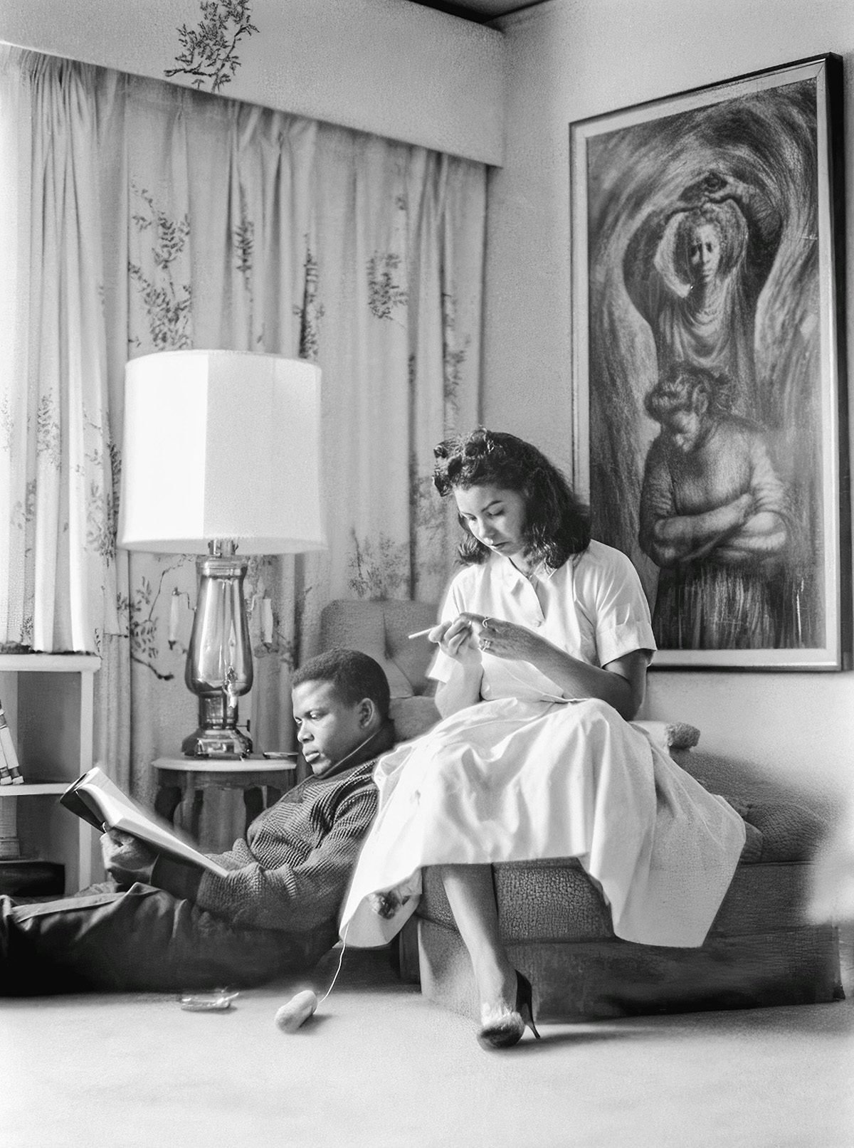 Black and white photo of Sidney Poitier and an actress sat reading and glancing down in a seating area