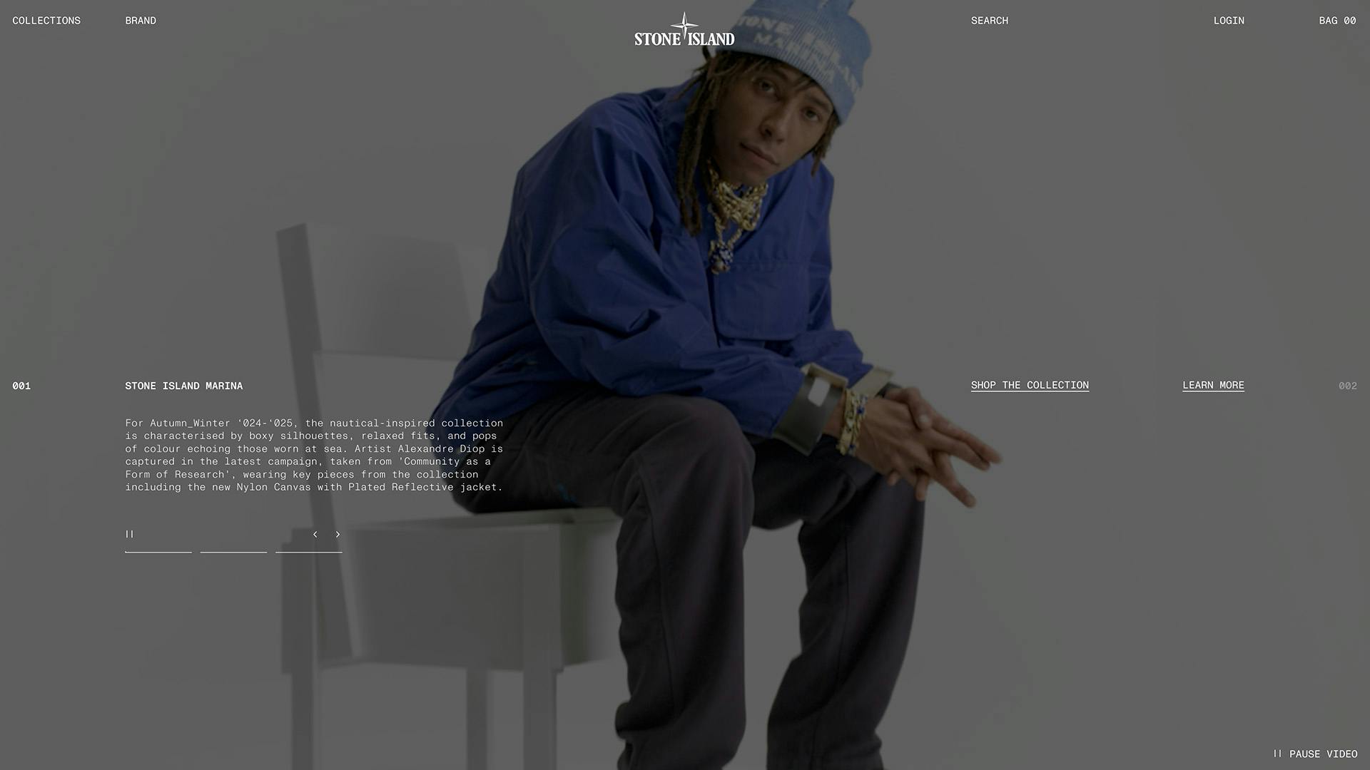 A man with braided hair wearing a blue Stone Island jacket and hat sat in a studio environment, shown on the Stone Island homepage