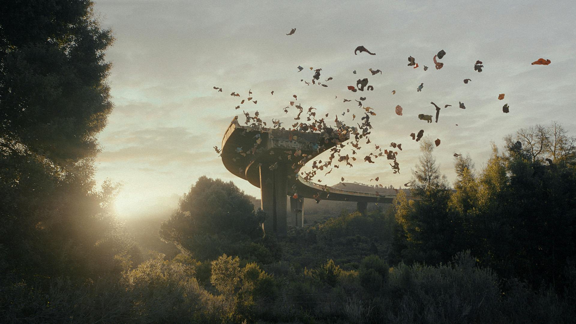 Pieces of clothing floating over an elevated motorway surrounded by trees, where the road is cut off to form a dead end