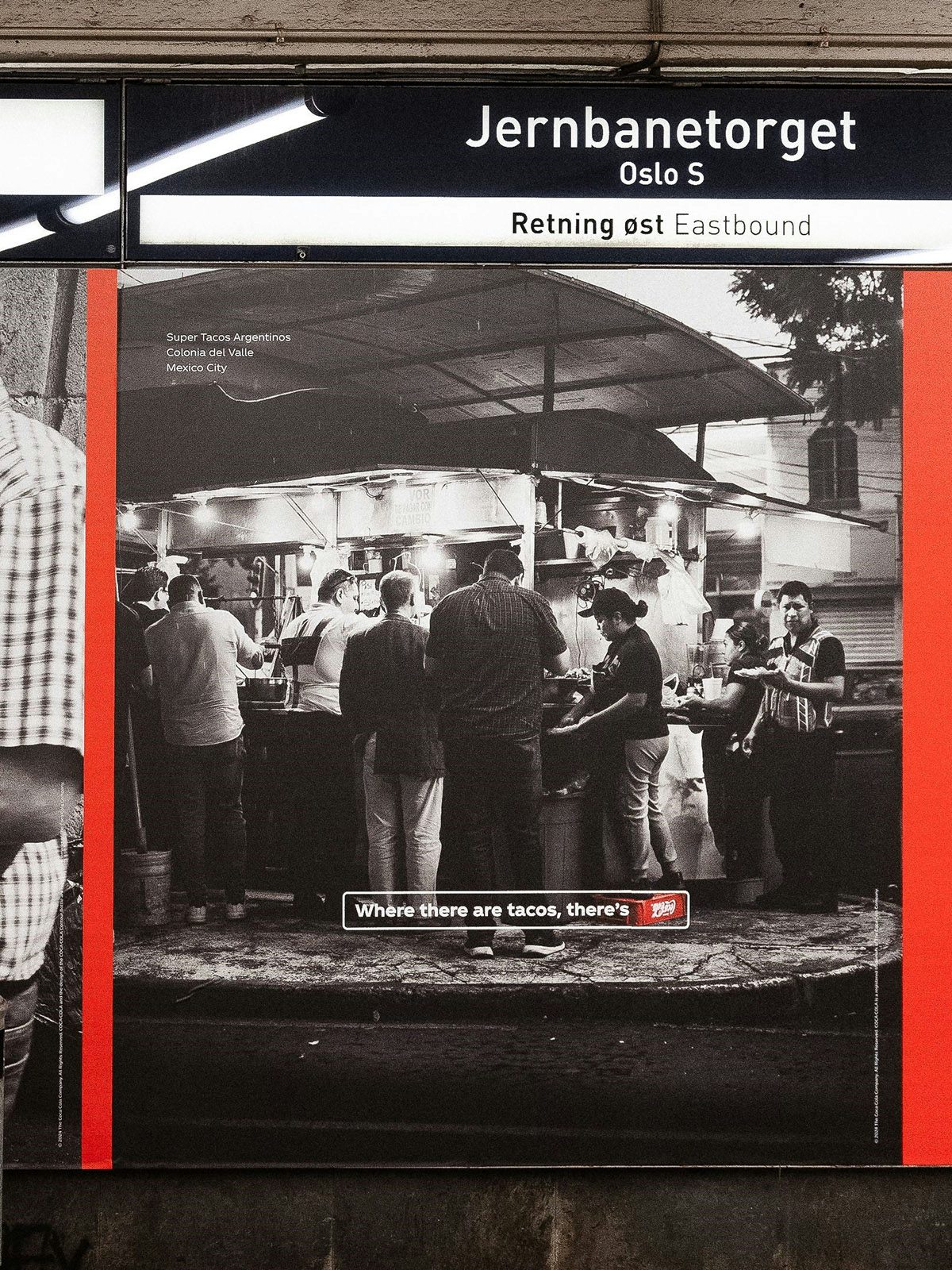 An outdoor ad featuring a black and white photo of a taco stall with a crate of Coca-Cola next to the stall highlighted in red