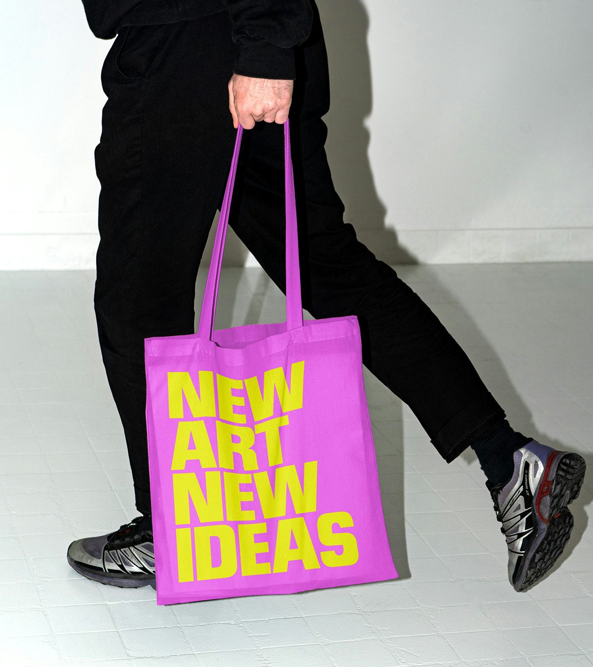 A person carrying a bright pink tote bag labelled 'new art new ideas' in bright yellow uppercase letters