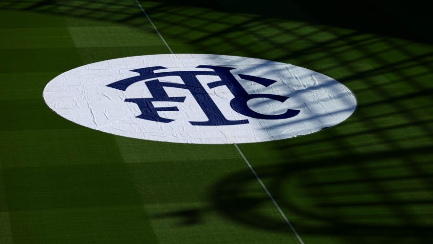 A navy and white Tottenham Hotspur monogram that reads 'THFC', shown on a banner displayed flat on a football pitch