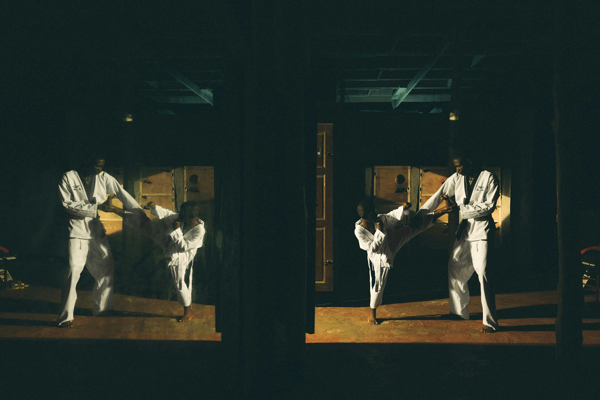 Photo by Carlos Idun-Tawiah showing a young person and an adult doing karate training in a low-lit space. The image is reflected to appear twice