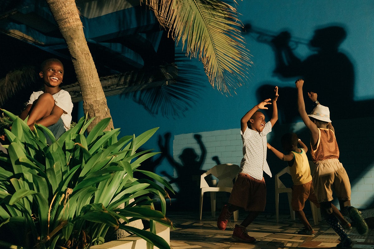 Photo by Carlos Idun-Tawiah showing young people dancing in a plant lined terrace with shadows of musicians cast on the wall behind them